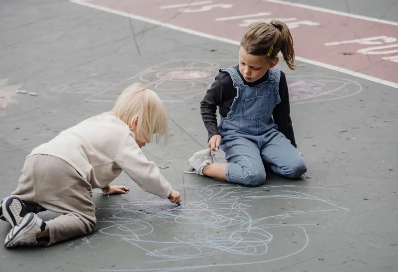 Two young children draw with chalk on an outdoor court